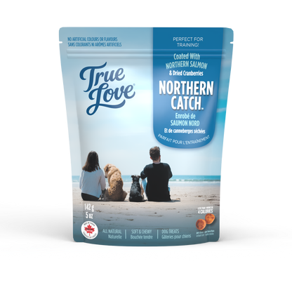 Bag of True Love dog treats with a family and their dogs on an ocean beach. Northern Catch flavour - northern salmon and dried cranberries.
